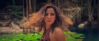 Movie still from “Queens on the Run” (2023), directed by Jorge Macaya – A beautiful woman with long brown hair in front of a forest; Close Up shot, Low angle