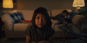 Movie still from “Quiz Lady” (2023), directed by Jessica Yu – A young girl sitting on the floor in front of a couch; Medium shot, Over the shoulder angle