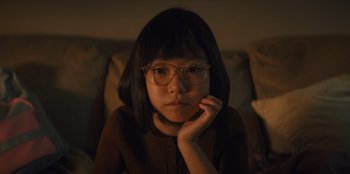 Movie still from “Quiz Lady” (2023), directed by Jessica Yu – A girl with glasses is sitting on a couch; Close Up shot, High angle