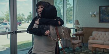 Movie still from “Quiz Lady” (2023), directed by Jessica Yu – Two women hugging in a living room with a window in the background; Close Up shot, Over the shoulder angle