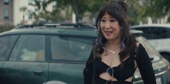 Movie still from “Quiz Lady” (2023), directed by Jessica Yu – A woman in a black dress standing in front of a car; Close Up shot, Over the shoulder angle