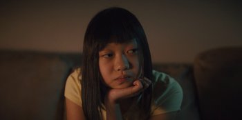 Movie still from “Quiz Lady” (2023), directed by Jessica Yu – A young asian woman sitting in a chair with her chin resting on her hand; Close Up shot, High angle