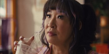 Movie still from “Quiz Lady” (2023), directed by Jessica Yu – A person with purple hair holding a drink; Close Up shot, Over the shoulder angle