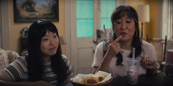 Movie still from “Quiz Lady” (2023), directed by Jessica Yu – Two women sitting at a table with a bowl of food; Close Up shot, Over the shoulder angle