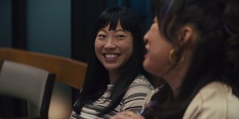 Movie still from “Quiz Lady” (2023), directed by Jessica Yu – Two women are sitting and smiling at a party; Close Up shot, Over the shoulder angle