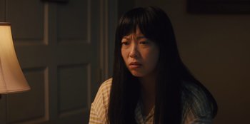 Movie still from “Quiz Lady” (2023), directed by Jessica Yu – A woman with long black hair sitting in front of a door; Close Up shot, Over the shoulder angle