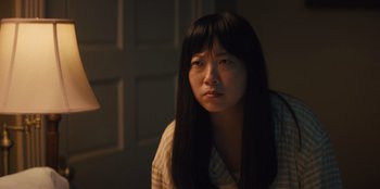 Movie still from “Quiz Lady” (2023), directed by Jessica Yu – A woman with long black hair sitting in a dimly - lit room; Close Up shot, Over the shoulder angle