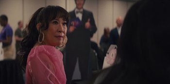 Movie still from “Quiz Lady” (2023), directed by Jessica Yu – A woman in a pink dress is looking at a man in a suit; Close Up shot, Over the shoulder angle