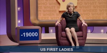 Movie still from “Quiz Lady” (2023), directed by Jessica Yu – A woman sitting on a purple chair in front of a tv; Medium shot, Over the shoulder angle