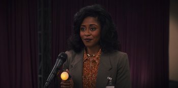 Movie still from “Quiz Lady” (2023), directed by Jessica Yu – A woman is holding a microphone in front of a microphone stand; Close Up shot, Over the shoulder angle