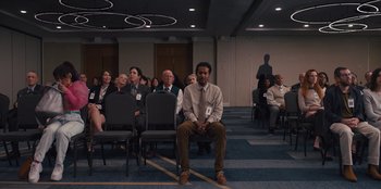 Movie still from “Quiz Lady” (2023), directed by Jessica Yu – A group of people sitting in a conference room; Wide shot, High angle