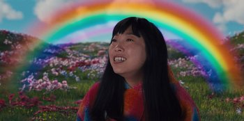 Movie still from “Quiz Lady” (2023), directed by Jessica Yu – A woman with long black hair smiles in front of a rainbow; Close Up shot, Low angle
