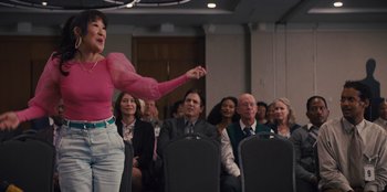 Movie still from “Quiz Lady” (2023), directed by Jessica Yu – A group of people sitting in a conference room; Medium shot, Over the shoulder angle