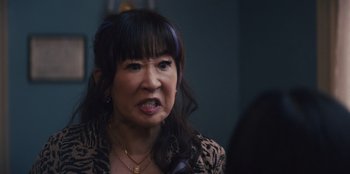 Movie still from “Quiz Lady” (2023), directed by Jessica Yu – An older woman with long black hair and a leopard print jacket; Close Up shot, Over the shoulder angle
