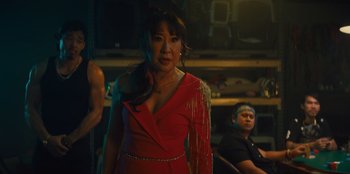 Movie still from “Quiz Lady” (2023), directed by Jessica Yu – A woman in a red dress standing next to a man in a black shirt; Medium shot, Over the shoulder angle