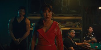 Movie still from “Quiz Lady” (2023), directed by Jessica Yu – A woman in a red dress standing next to a man; Medium shot, Low angle