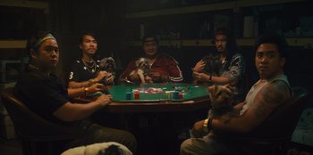 Movie still from “Quiz Lady” (2023), directed by Jessica Yu – A group of people sitting around a table with dogs; Wide shot, High angle