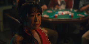 Movie still from “Quiz Lady” (2023), directed by Jessica Yu – A woman sitting in front of a green table; Close Up shot, Over the shoulder angle