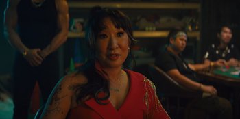 Movie still from “Quiz Lady” (2023), directed by Jessica Yu – A woman in a red dress is posing for a picture; Close Up shot, Over the shoulder angle