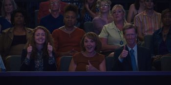Movie still from “Quiz Lady” (2023), directed by Jessica Yu – A group of people sitting in a row at a concert; Medium shot, High angle