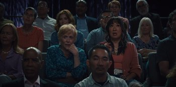 Movie still from “Quiz Lady” (2023), directed by Jessica Yu – A group of people sitting in front of each other; Medium shot, Over the shoulder angle