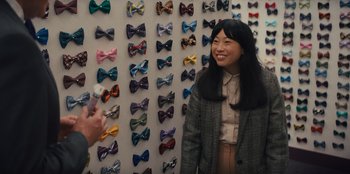 Movie still from “Quiz Lady” (2023), directed by Jessica Yu – A woman standing in front of a wall covered with many ties; Medium shot, Over the shoulder angle