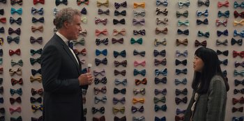 Movie still from “Quiz Lady” (2023), directed by Jessica Yu – A man standing in front of a wall of bow ties; Medium shot, Over the shoulder angle