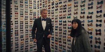 Movie still from “Quiz Lady” (2023), directed by Jessica Yu – A man and a woman standing in front of a wall covered in bow ties; Medium shot, Over the shoulder angle