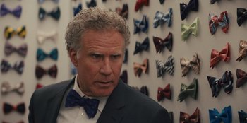 Movie still from “Quiz Lady” (2023), directed by Jessica Yu – A man in a suit and a bow tie in front of a wall of bow ties; Close Up shot, Over the shoulder angle