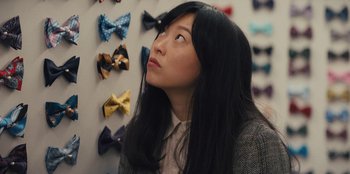 Movie still from “Quiz Lady” (2023), directed by Jessica Yu – A woman standing in front of a wall of bows; Close Up shot, Over the shoulder angle