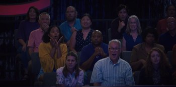 Movie still from “Quiz Lady” (2023), directed by Jessica Yu – A group of people sitting and standing in front of each other; Medium shot, High angle