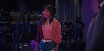 Movie still from “Quiz Lady” (2023), directed by Jessica Yu – A woman in a pink shirt and blue jeans; Medium shot, Over the shoulder angle