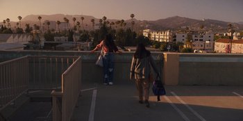 Movie still from “Quiz Lady” (2023), directed by Jessica Yu – Two women are walking on a bridge over a river; Extreme Wide shot, Low angle