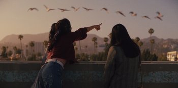 Movie still from “Quiz Lady” (2023), directed by Jessica Yu – A woman pointing at a flock of birds flying in the sky; Medium shot, Over the shoulder angle