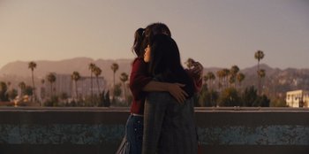 Movie still from “Quiz Lady” (2023), directed by Jessica Yu – A group of people hugging in front of a sky background; Medium shot, Over the shoulder angle