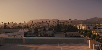 Movie still from “Quiz Lady” (2023), directed by Jessica Yu – A parking lot with palm trees in the background; Extreme Wide shot, High angle