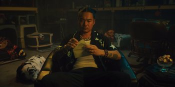 Movie still from “Quiz Lady” (2023), directed by Jessica Yu – A man sitting in a chair looking at a piece of paper; Medium shot, Low angle