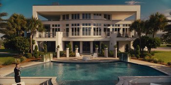 Movie still from “Quiz Lady” (2023), directed by Jessica Yu – A large swimming pool in front of a large building; Extreme Wide shot, High angle