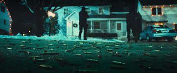 Movie still from “RED” (2010), directed by Robert Schwentke – A man standing in front of a house covered in bullet casings; Extreme Wide shot, Low angle
