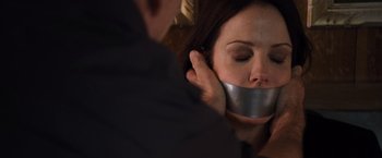 Movie still from “RED” (2010), directed by Robert Schwentke – A woman with her mouth taped shut by a man with his hand on her face; Close Up shot, Over the shoulder angle