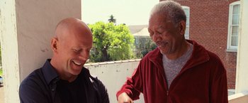 Movie still from “RED” (2010), directed by Robert Schwentke – Two men are laughing together on a balcony; Medium shot, Low angle