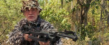Movie still from “RED” (2010), directed by Robert Schwentke – A man holding a crossbow while wearing a hat; Medium shot, Over the shoulder angle