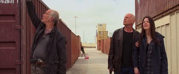 Movie still from “RED” (2010), directed by Robert Schwentke – Two men standing on a sidewalk with a skatebaord in the background; Medium shot, Low angle