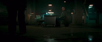 Movie still from “RED” (2010), directed by Robert Schwentke – A man sitting at a desk in a dark room; Wide shot, Low angle