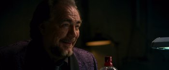 Movie still from “RED” (2010), directed by Robert Schwentke – An older man sitting next to a bottle of alcohol; Close Up shot, Over the shoulder angle