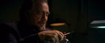 Movie still from “RED” (2010), directed by Robert Schwentke – An older man holding a needle and a bottle of wine; Close Up shot, Low angle