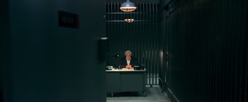 Movie still from “RED” (2010), directed by Robert Schwentke – An older man sitting at a desk in a jail cell; Wide shot, High angle