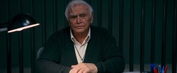 Movie still from “RED” (2010), directed by Robert Schwentke – An older man sitting in front of a curtain; Close Up shot, Low angle