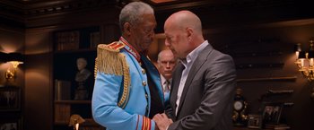 Movie still from “RED” (2010), directed by Robert Schwentke – A man in a suit and tie shaking hands with an older man in a suit; Medium shot, Low angle