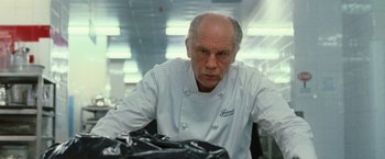 Movie still from “RED” (2010), directed by Robert Schwentke – An older man wearing a chef's outfit and looking at the camera; Close Up shot, Low angle